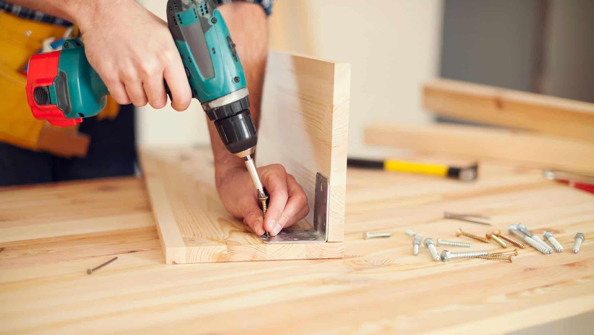 Person skrur sammen treplater med drill på arbeidsbenk.
