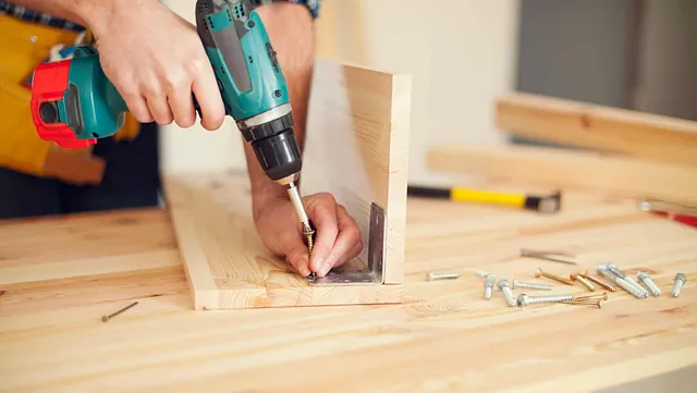 Person skrur sammen treplater med drill på arbeidsbenk.