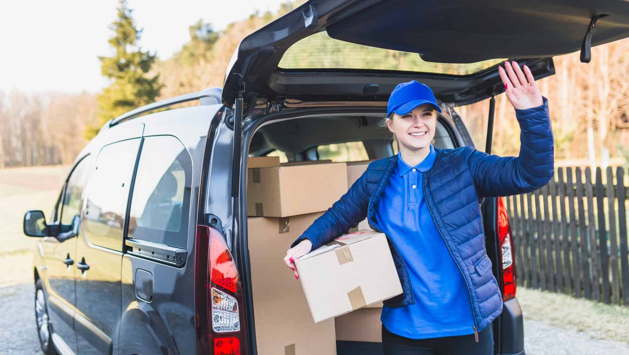 Smilende bud leverer esker fra bil og hilser med hånden.