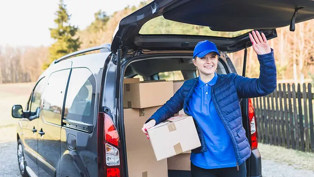 Smilende bud leverer esker fra bil og hilser med hånden.