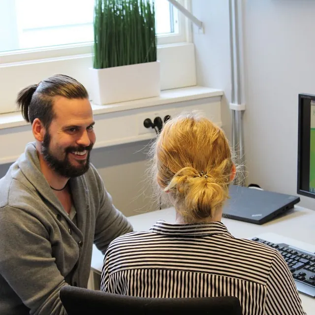 To personer sitter ved PC-skjerm og diskuterer arbeidsinteresser.