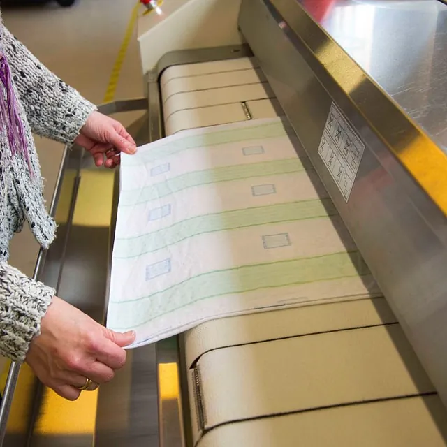 Person mater tekstil inn i industrielt vaskeri- og presseutstyr.