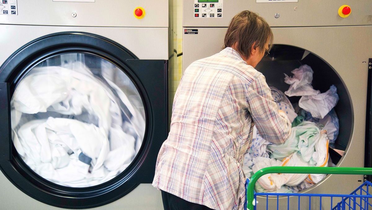 Person fyller store industrivaskemaskiner med hvitt tøy.