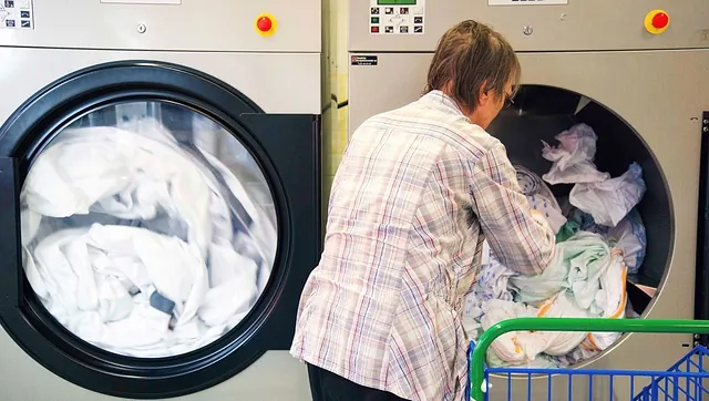 Person fyller store industrivaskemaskiner med hvitt tøy.