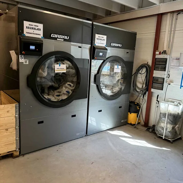 To store tørketromler fylt med klær i et vaskerom.