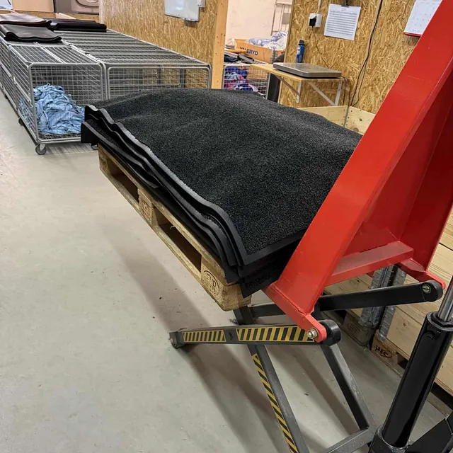 Løftevogn med pall lastet med sorte matter i et vaskerom.