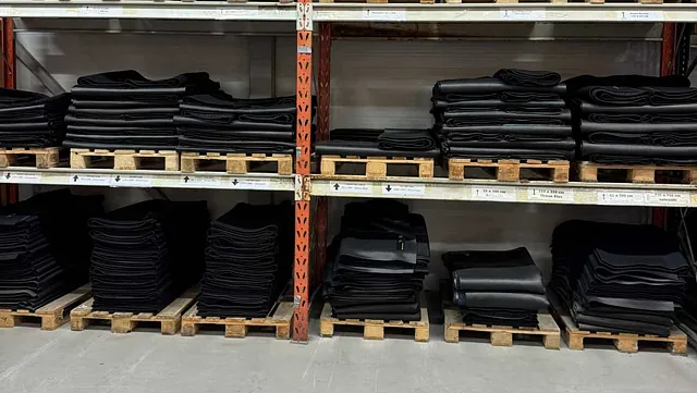 Reoler med stabler av sorte matter stablet på trepaller i et lager.